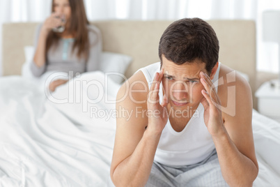 Man having a headache sitting on the bed with his girlfriend