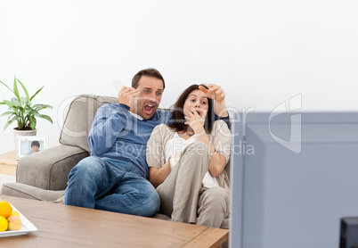 Scared couple watching a horror movie on the television
