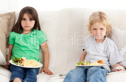 Serious brother and sister having dinner on the sofa