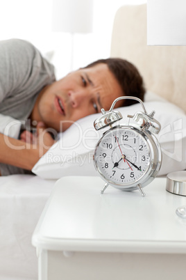 Unhappy man looking at his alarm clock while lying on his bed