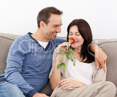 Lovely man looking at his girlfriend smelling a red rose