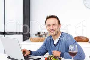 Happy man looking at his laptop while eating a salad