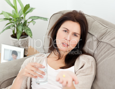 Tired woman taking her medicine lying on the sofa