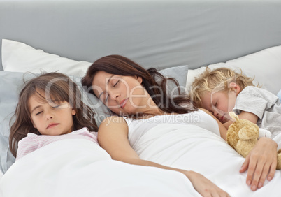 Adorable children sleeping with their mother on her bed