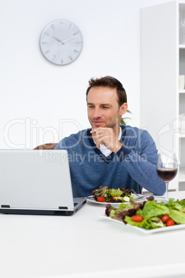 Handsome man looking at his laptop while having lunch