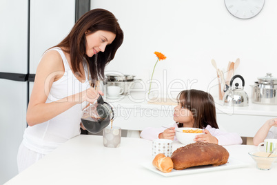 Pretty mom pouring coffee while her children having breakfast