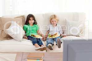 Cute brother and sister having dinner on the sofa
