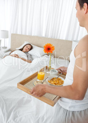 Lovely man bringing the breakfast to his girlfriend lying on the