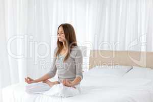 Pretty woman doing yoga exercises sitting on her bed