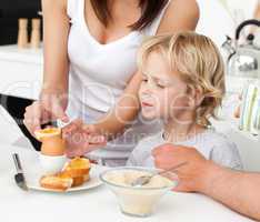 Attentive mother breaking a boiled egg for her son during breakf