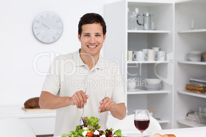 Happy man preparing a salad while drinking red wine