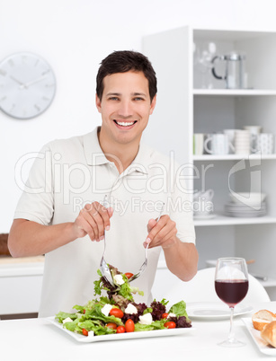 Happy man mixing a salad standing in the kitchen