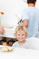 Happy boy eating boiled egg and bread in the kitchen