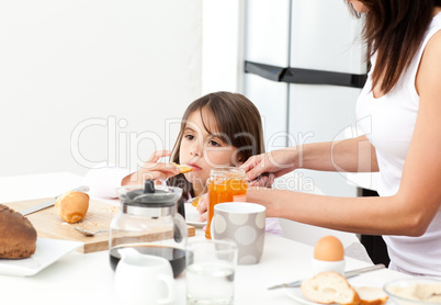 Pretty mother giving toast with jam to her daughter for the brea