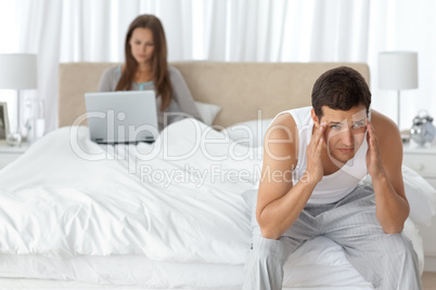 Man having a headache in the bedroom with his girlfriend
