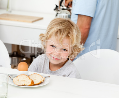 Little boy eating boiled egg and bread at breakfast