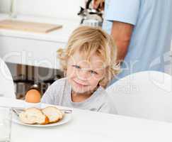 Little boy eating boiled egg and bread at breakfast