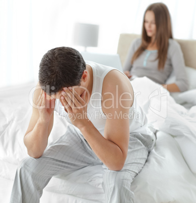 Stressed man sitting on his bed while his girlfriend working on