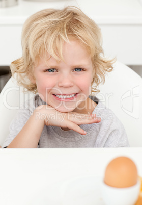 Cute little boy sitting at a table to eat a boiled egg
