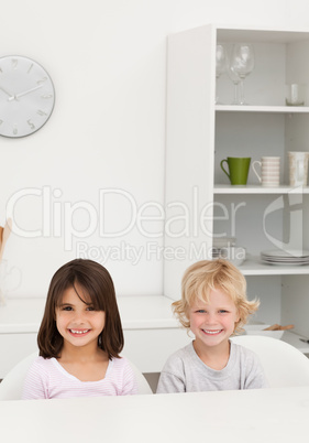 Little brother and sister smiling sitting at a table in the kitc