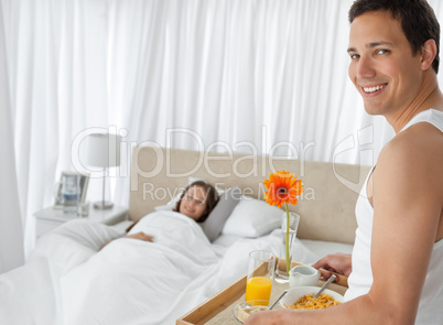 Happy man bringing the breakfast to his girlfriend on the bed