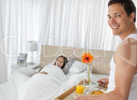 Happy man bringing the breakfast to his girlfriend on the bed