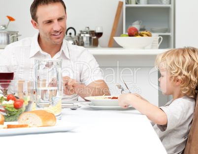 Happy dad looking at his son eating pasta