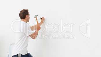 Rear view of a man hammering against a white wall