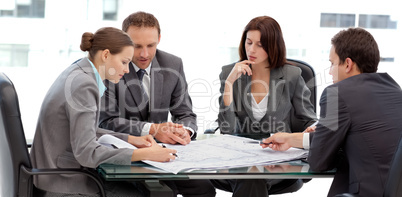 Four serious engineers looking at plans sitting at a table