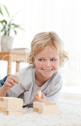 Cute little boy playing with dominoes lying on the floor