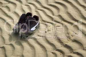 Schuhe am Strand mit Wasserrillen im Sand
