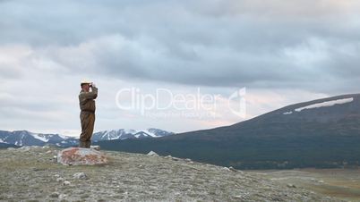 Hiker in mountain look into binoculars