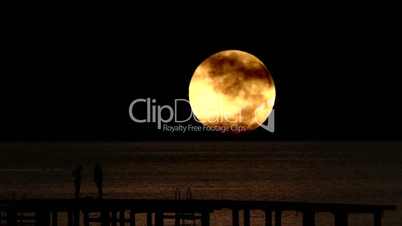 Young couple silhouetted on pier against timelapse full moon