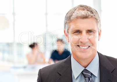 Businessman looking at the camera while their team is working