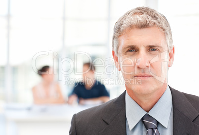 Businessman looking at the camera while his team is working