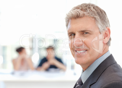 Businessman looking at the camera while the team is working