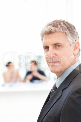 Businessman looking at the camera while his team is working