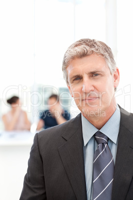 Businessman looking at the camera while his team is working