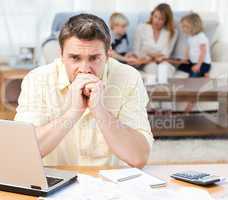 Man calculating his bills while his family are on the sofa