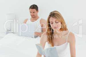 Man is on his laptop while his wife is reading a book