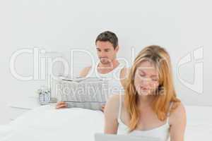 Woman is on her laptop while her husband is reading newspaper