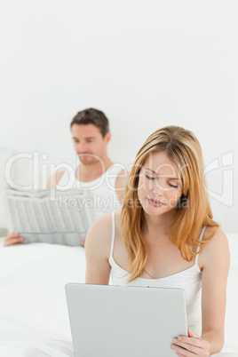 Woman is on her laptop while her husband is reading newspaper