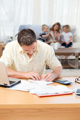 Man calculating his bills while his family are on the sofa