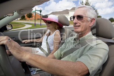 Senior Couple Driving Convertible Car Wearing Sunglasses