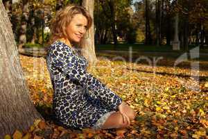 woman sit and smile on ground in autumn leaves