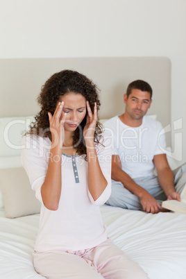 Woman having a headache while her husband is reading