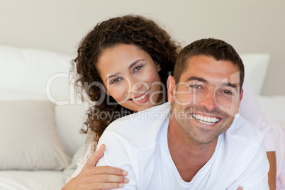 Pretty woman hugging her husband on their bed at home
