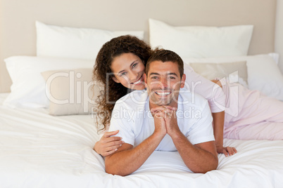 Pretty woman hugging her husband on their bed at home