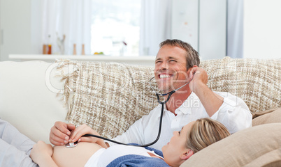 Man listening his wife's belly with his stethoscope