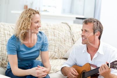 Romantic man playing guitar for her wife at home